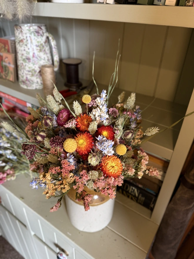 a dried flower bouquet in bright spring/summer colours in a victorian jam pot sitting on a green painted dresser