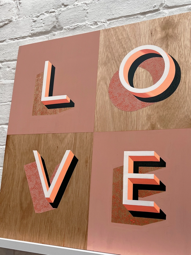 LOVE hand painted sign in pinks and neon orange, against a white brick wall, at an angle. 