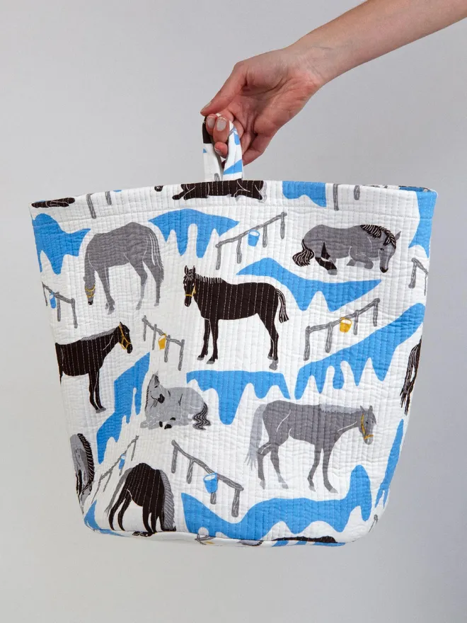 Horse Ranch Quilted Storage Basket, a person holding a blue horse print basket against a grey backdrop. 