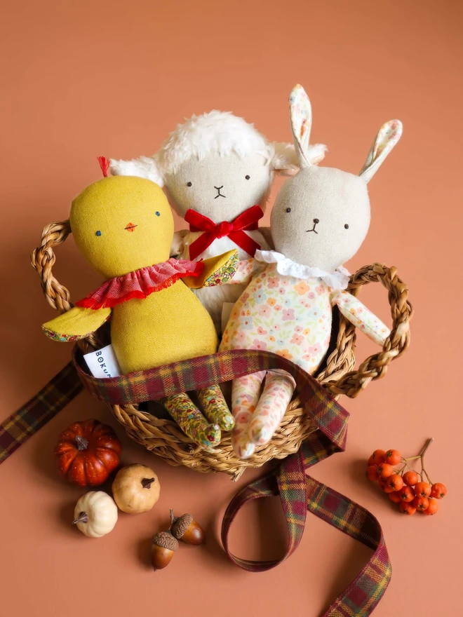Handmade chick doll made from soft yellow fabric, with a stitched face, small beak, ruffled collar, and patterned fabric arms and long legs, with fluffy white lamb doll and floral bunny doll.