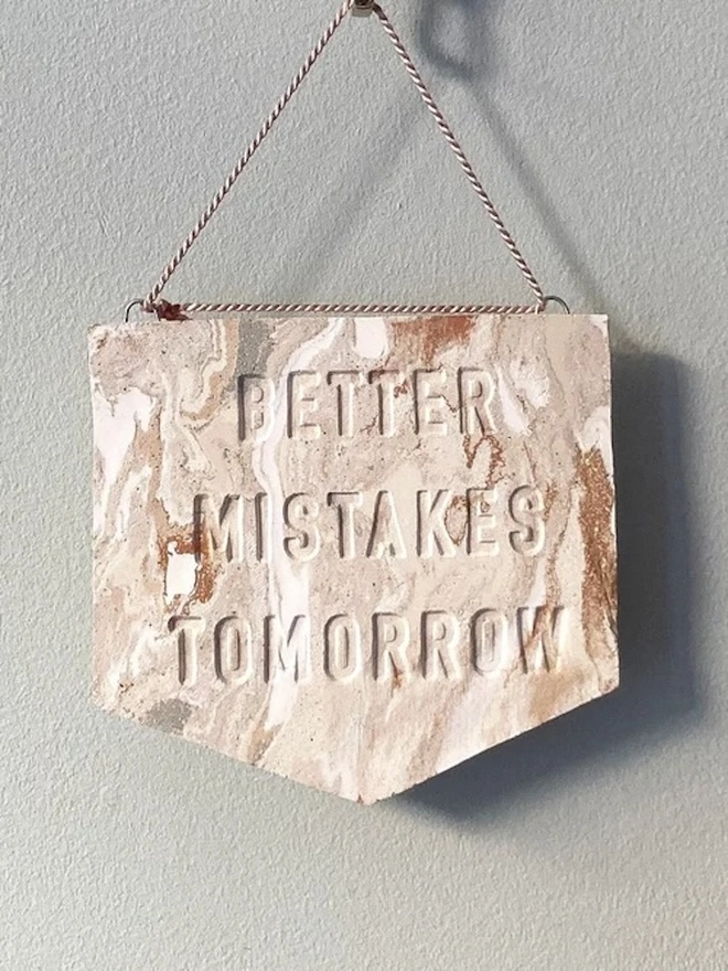 'Better Mistakes Tomorrow' Banner, a clay banner hanging against a plain backdrop.