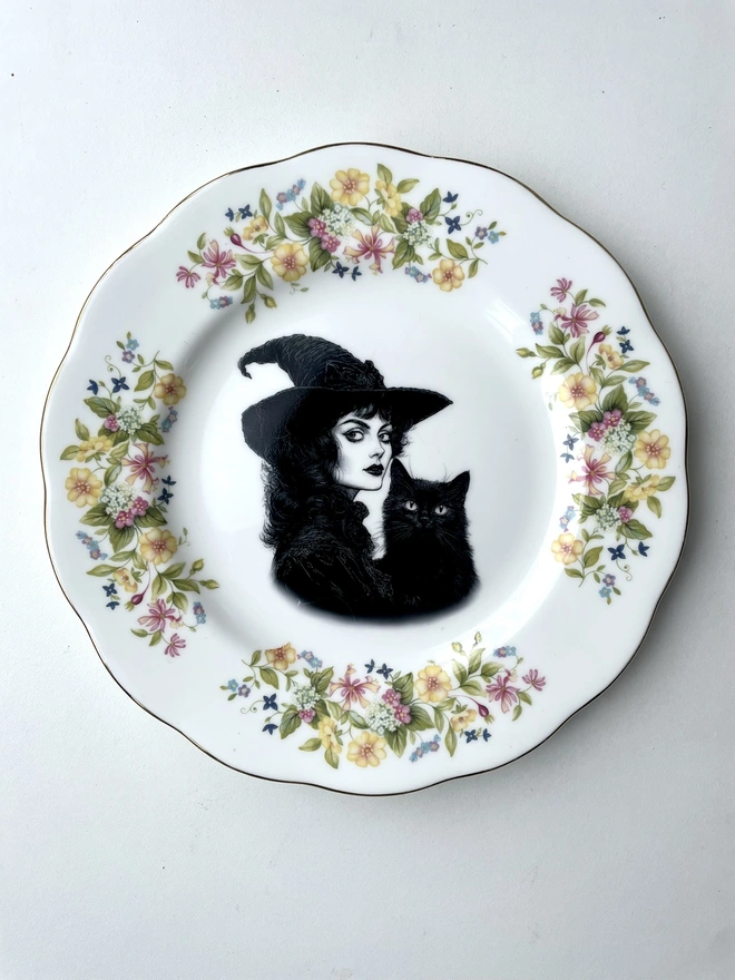 vintage plate with an ornate border, with a printed vintage illustration of a Victorian witch and her black cat in the middle