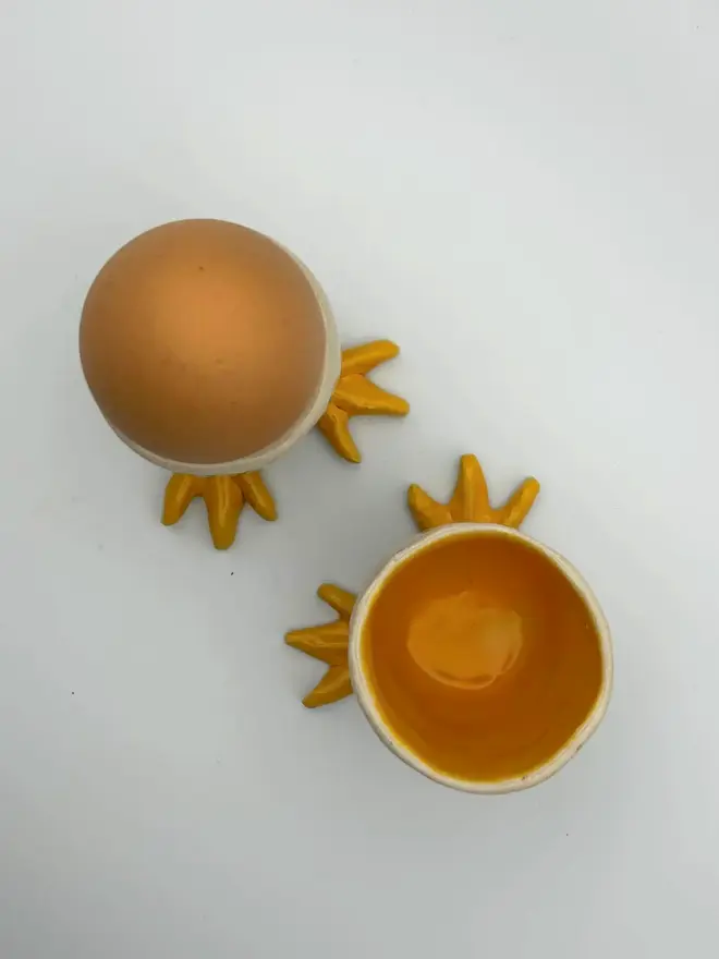 What Came First The Chicken Or The Egg… Cup , a pair of egg cups on a plain surface. One has an egg in it. 