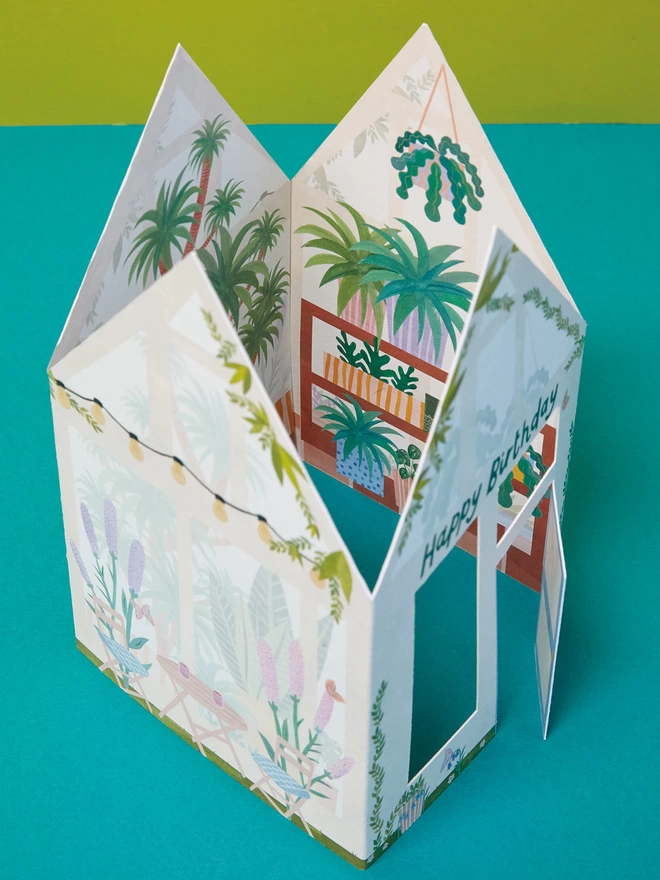 A view from above showing the inside of the 3D greenhouse 'Happy Birthday' card reveals the intricate inside design, filled with tropical plants, hanging baskets, and painted colourful pots.