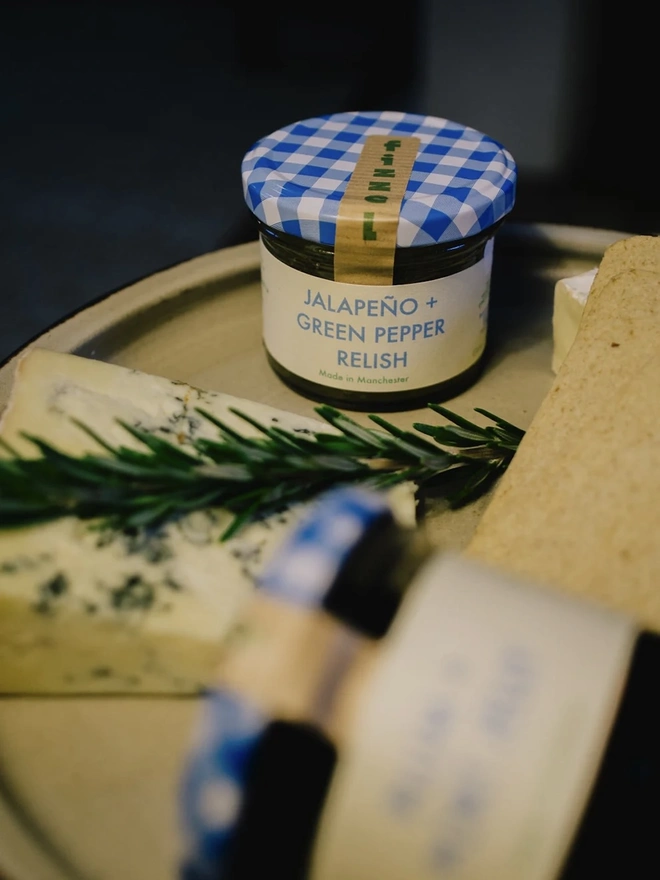 Jar Of Jalapeño & Green Pepper Relish, jar of relish on a tray, next to herbs. 