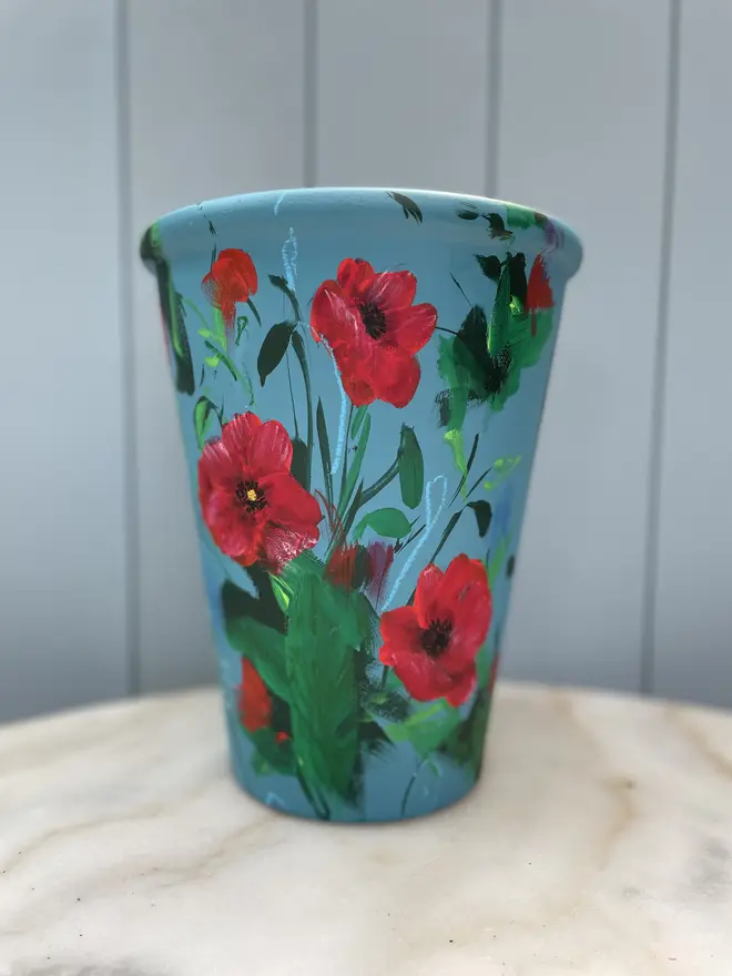 Unique hand-painted terracotta pot featuring red poppies on a royal blue background