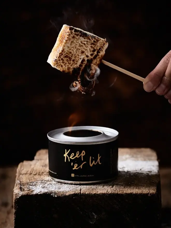 Vanilla Bean Jumbo Mallows (Pack Of 4), a marshmallow being burnt over a fire. It is skewered by a stick and is going brown. 