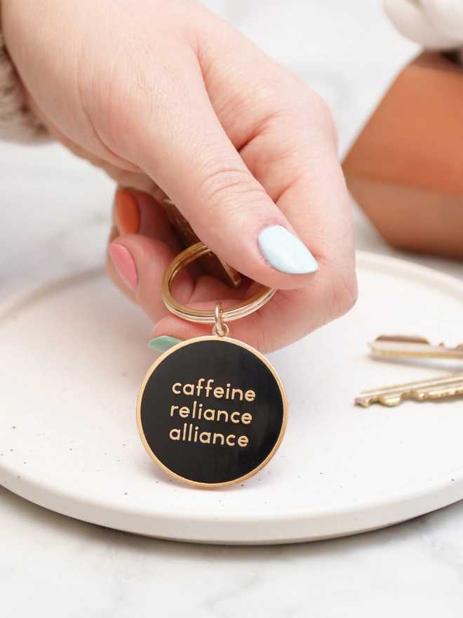 Hand holding a Caffeine reliance alliance enamel keyring 