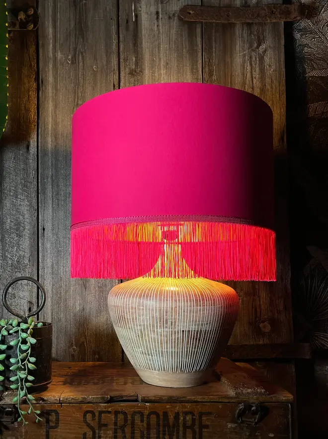 Pomegranate Pink Lampshade With Gold Lining & Pink Fringing, on a table. 