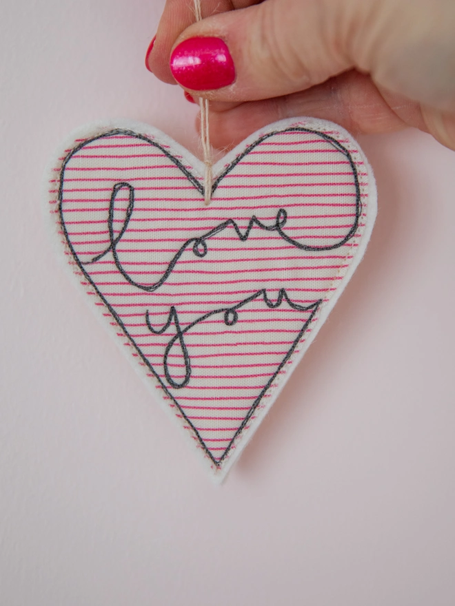 Love you embroidered Valentine's Day heart. A heart shaped hanging decoration in a red striped fabric with the words I love you embroidered on the front.