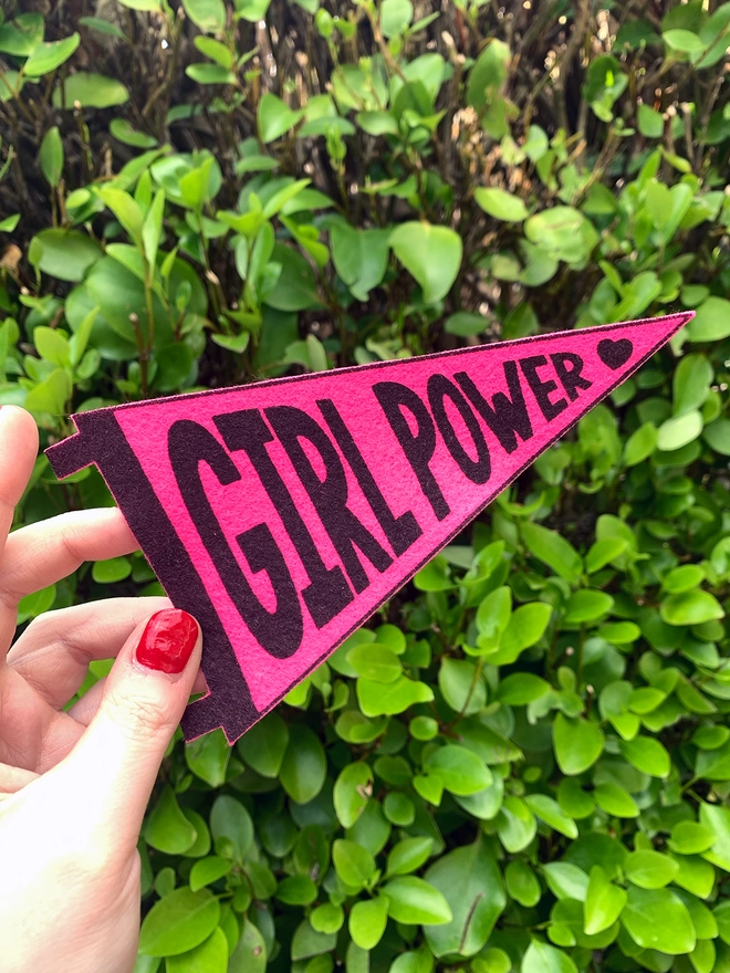 image shows a hand holding a bright pink felt pennant with the words ‘girl power’ printed on in black ink.