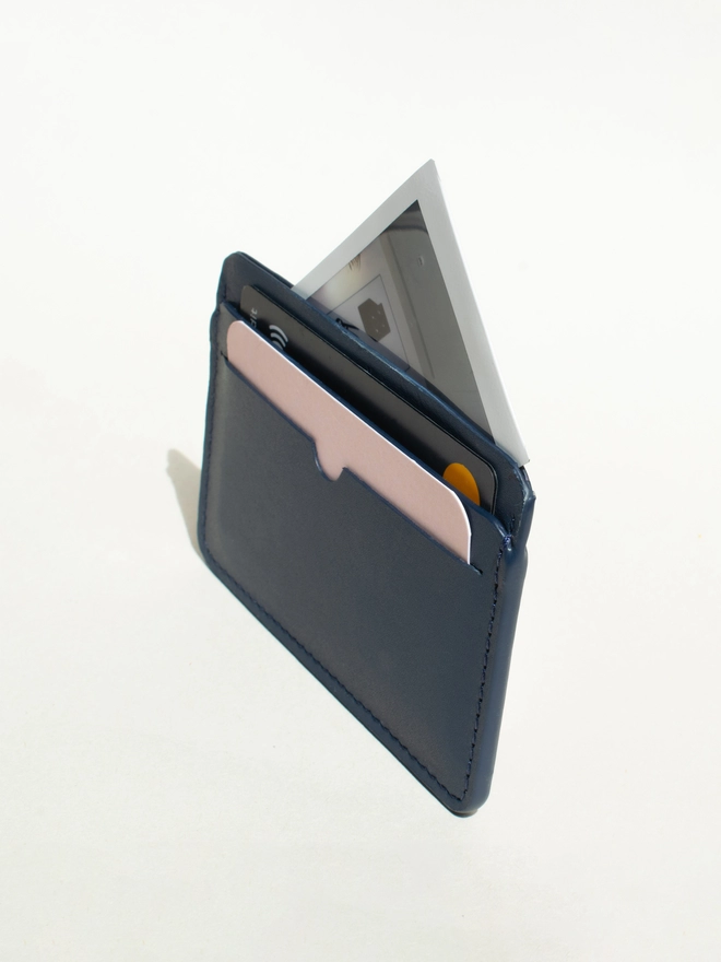 navy cardholder standing at an angle. The card has 2 cards in the slots and a poloroid photo in the middle