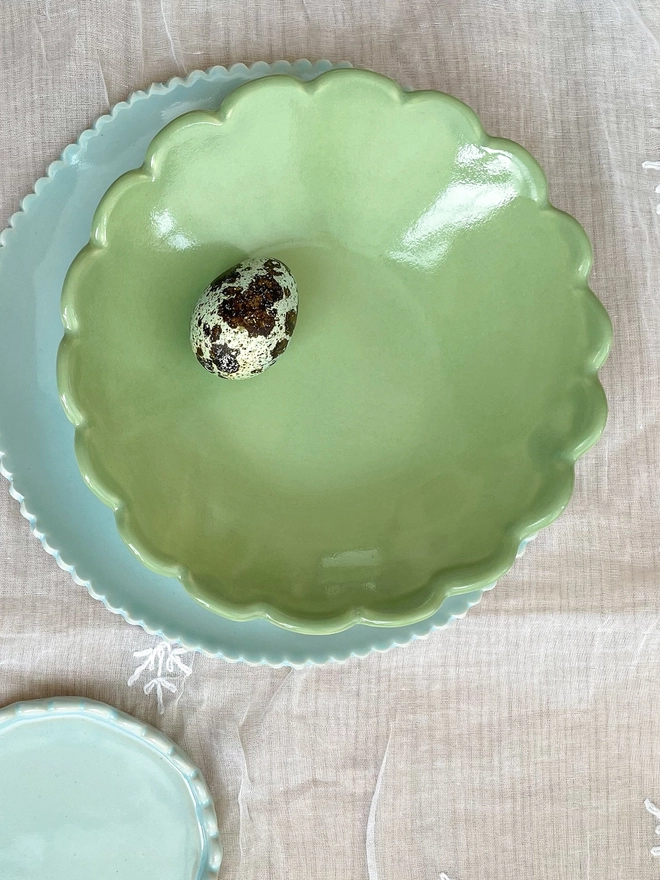 top view of camellia edge ice cream bowl in sage green sittting on a light blue scalloped edge side plate