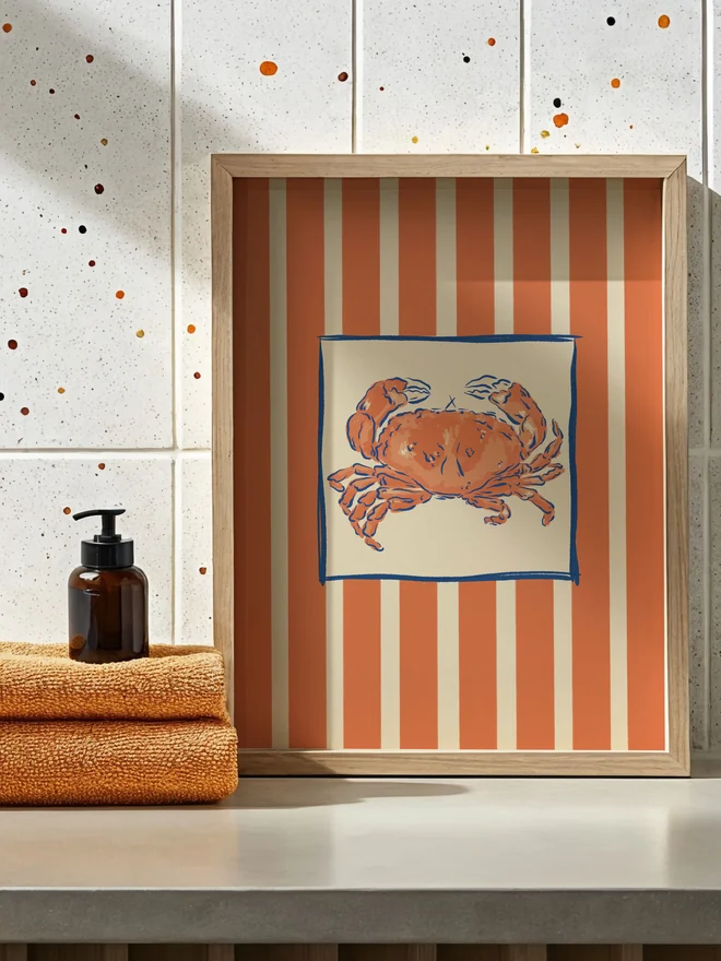 Crab stripe art print in a bathroom next to matching orange towels. 