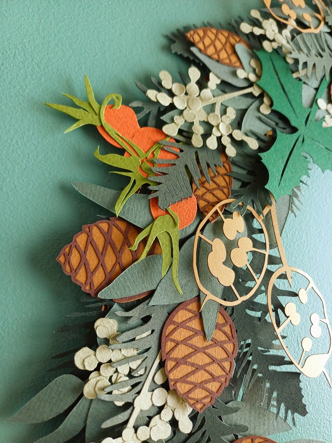 Detail of paper pinecones, rosehips, seeded eucalyptus and holly on papercut wreath