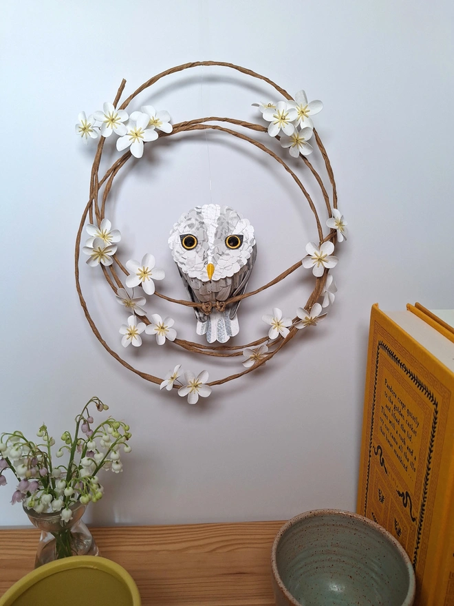 Great grey owl baby sculpture wall hanging. The owl paper sculpture is perched on a floral wreath of white and yellow flower blossoms