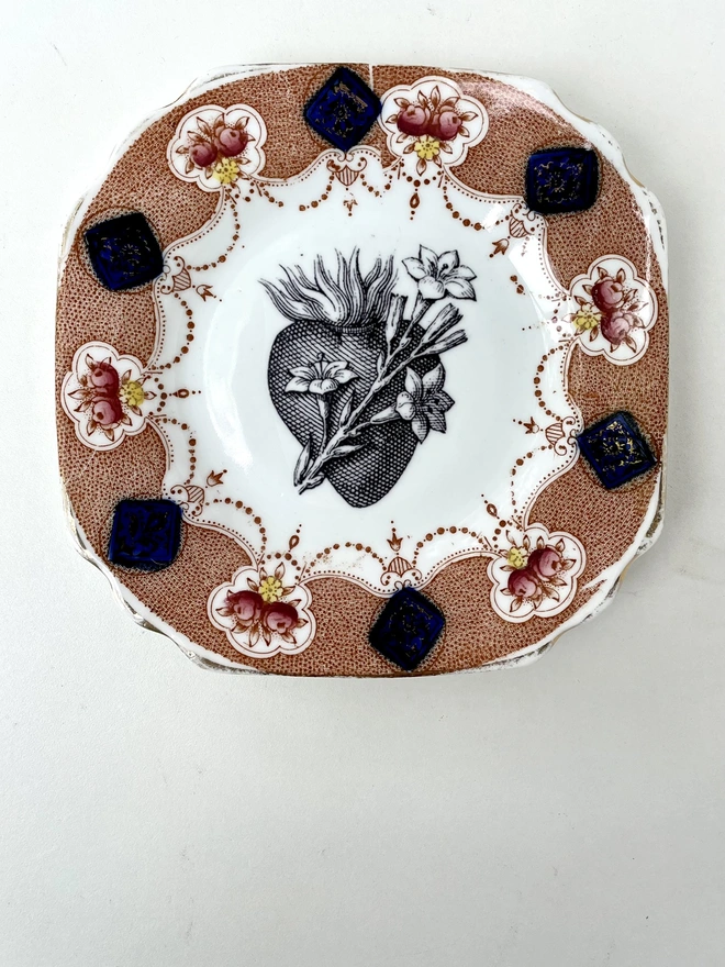 a vintage plate with an ornate border and in the centre is an old illustration of a beautiful sacred heart