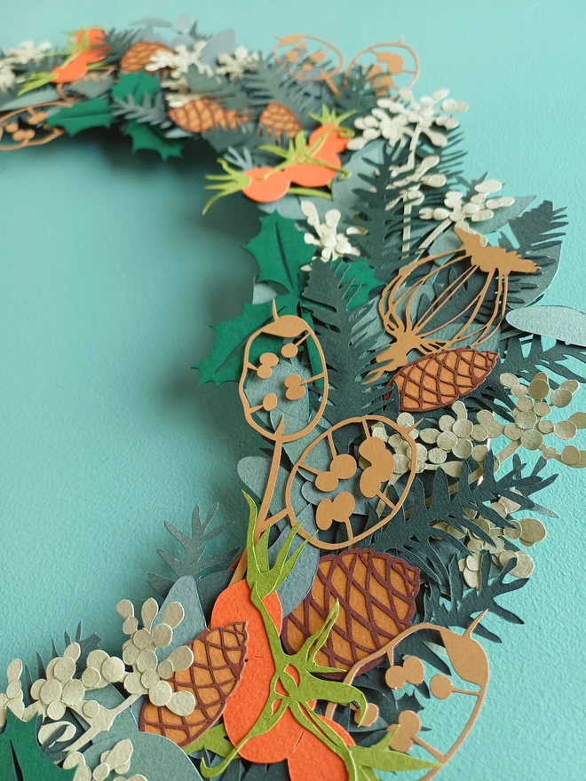 Close detail view of papercut wreath showing gold honesty seedhead, spruce, pinecones, seeded eucalyptus and rosehips