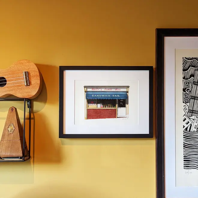 Clerkenwell Scotti's Snack Bar Giclée Print (Unframed), a print of a snack bar sitting in a black frame on a mustard backdrop joined by other framed prints. 