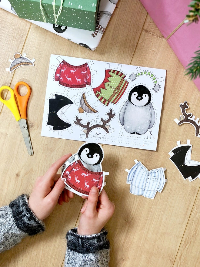 A child is playing with a dress up penguin paper doll that has been cut from a Christmas greetings card.