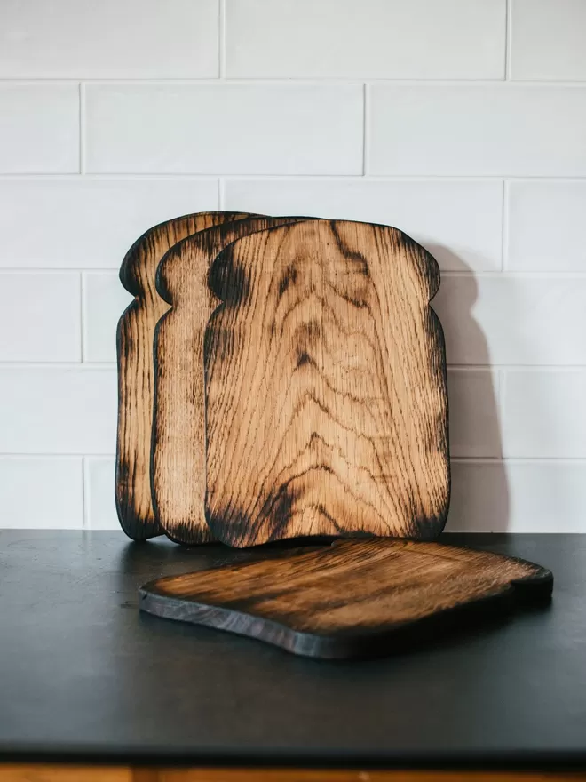 ‘That Feeling Of Home!’ Toast Shaped Oak Serving Board seen on a kitchen countertop.