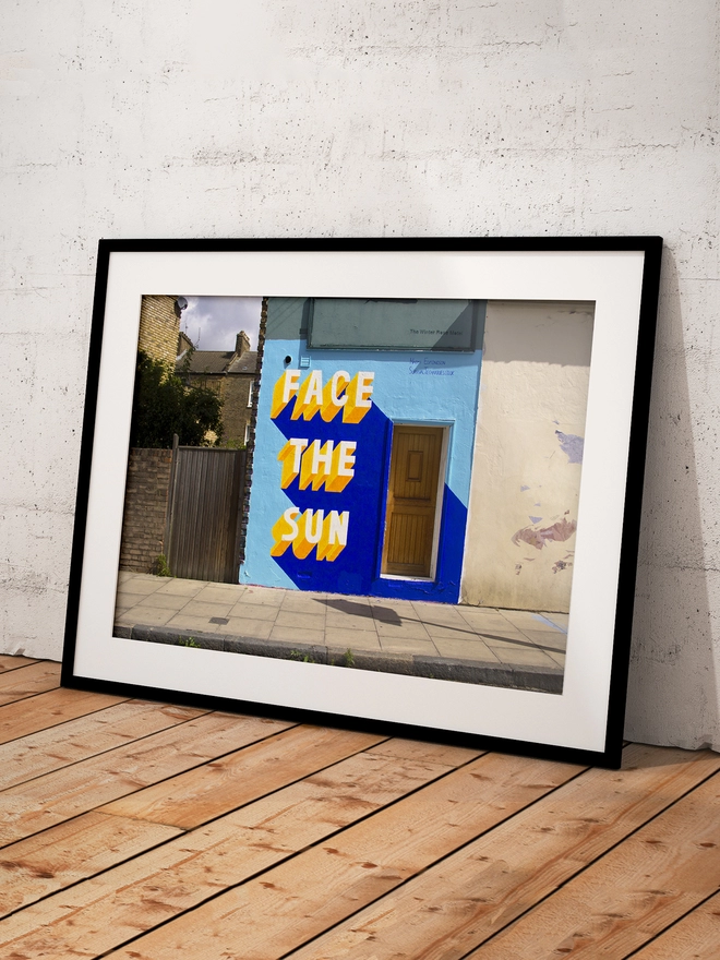 Framed art print of street art by Survival Techniques with the words Face The Sun in 3d typography on a wall