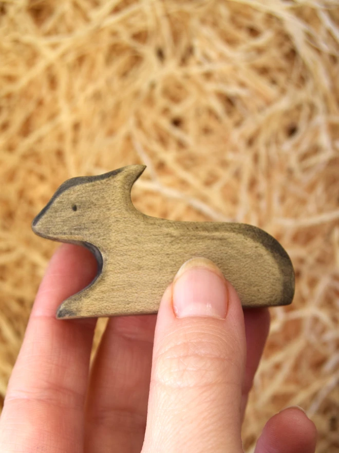 black lamb lying down wooden toy in hand above woodwool