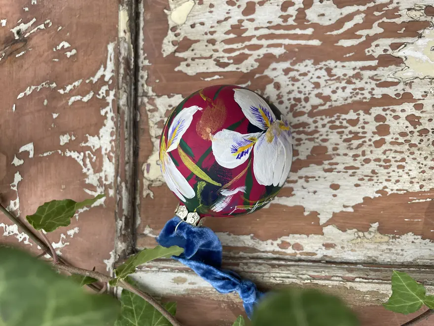 Hand painted floral ceramic christmas bauble dark pink background with Algerian winter iris flowers.