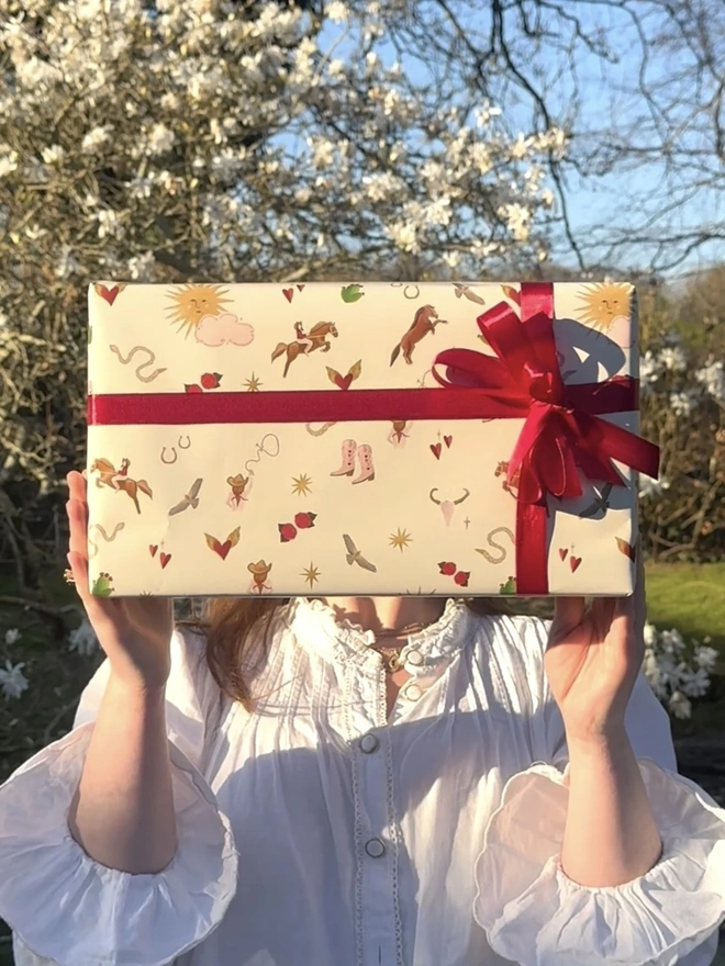 Wild Rodeo Gift Wrap (3 Sheets), a person holding up a gift, with the wrapping paper. 