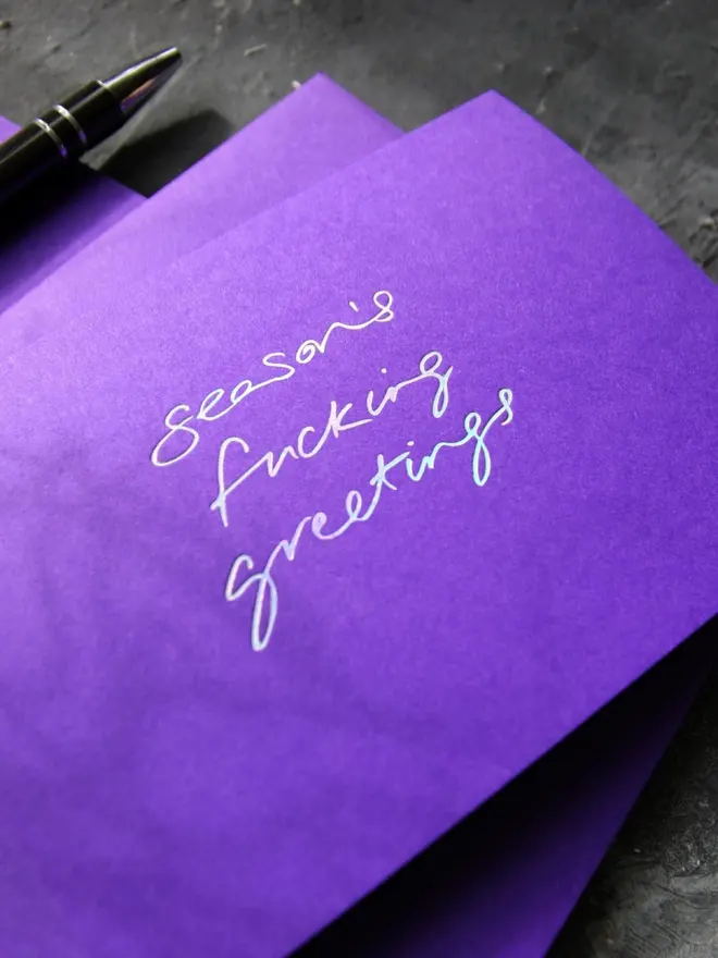 Hand foiled cash card or money wallet in a royal purple colour handfoiled in shiny holographic text which says 'season's fucking greetings'.