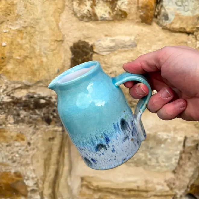 Shoreline Medium Jug, a colourful jug being poured against a brick wall backdrop. 