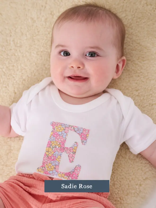 a baby wearing a personalised cotton bodysuit with her initial on in floral liberty print