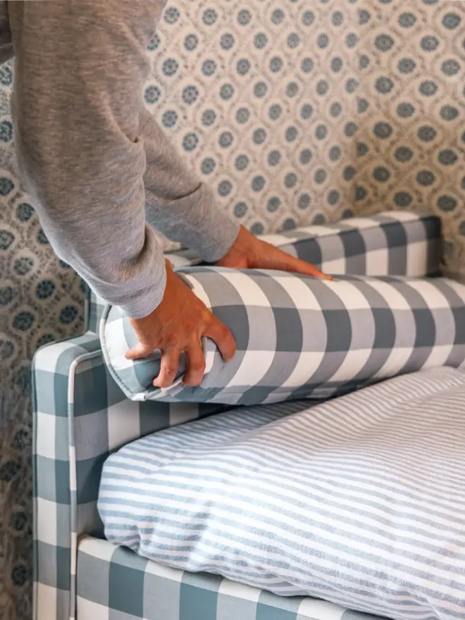 'The Posie' blue gingham upholstered children's bed. a blue gingham sofa-style bed for children featuring a bolster cushion being placed onto the mattress. 