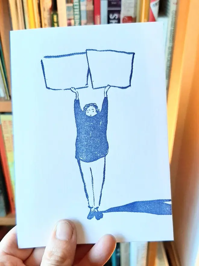 Blank Message Letterpress Handprinted Greetings Card, a person holding the white greetings card with a blue design in front of a book shelf. 