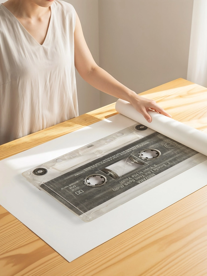 Nirvana 'Smells Like Teen Spirit cassette tape print. artist unrolling print on studio desk.