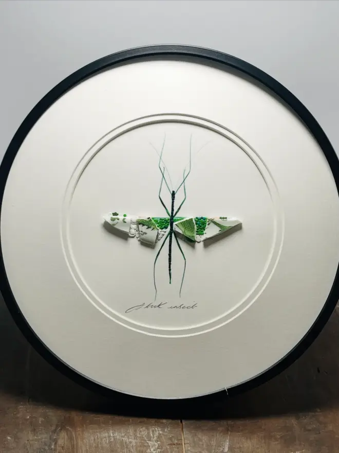 Hand-drawn, painted, mosaic clay, vintage green Dragon pottery insect on white double mounted card, in a black circular frame.
