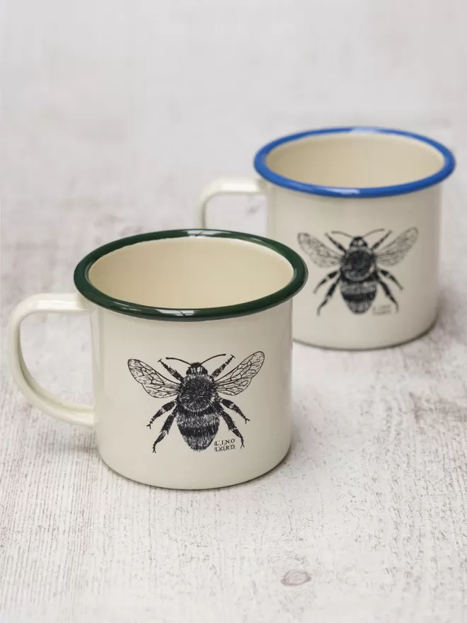 Picture of 2 Cream Enamel Mug with a Green Rim and Blue Rim with a Bee design etched onto it, taken from an original Lino Print