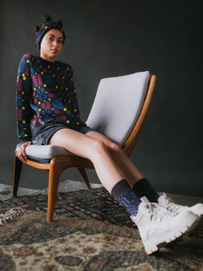 Model wearing pieces from MABLI's 'Carthen' collection, featuring the Carthen Jumper in the vibrant 'Fireworks' colour-way. The design showcases bold, colourful patterns inspired by traditional Welsh blanket tapestry.