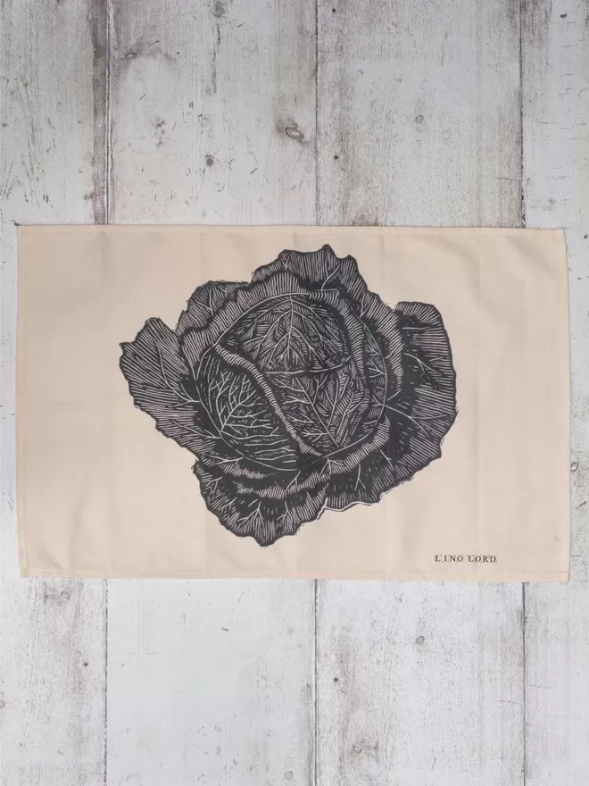 Picture of a tea towel with an image of a savoy cabbage, taken from an original lino print