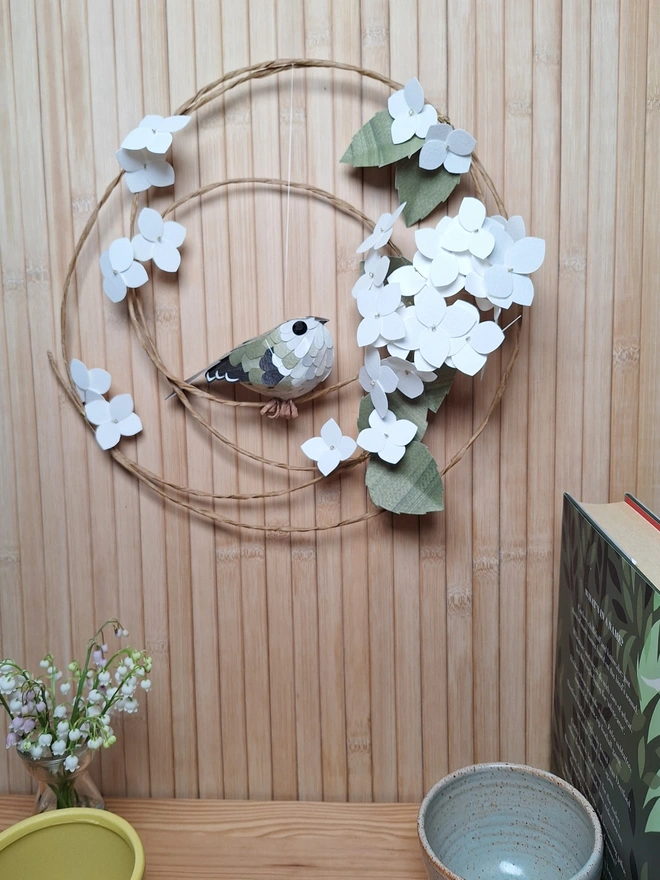 Handmade paper wall art of a goldcrest perched on a white hydrangea floral wreath