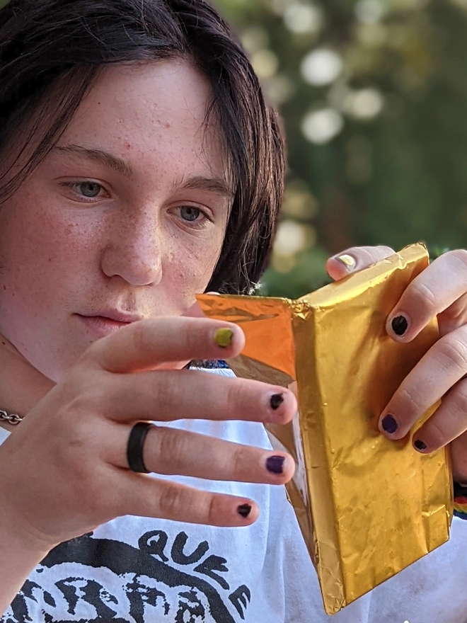 Happy young teenager opening gold foil wrapped charity milk chcoclate with cheesecake gingernut crunch