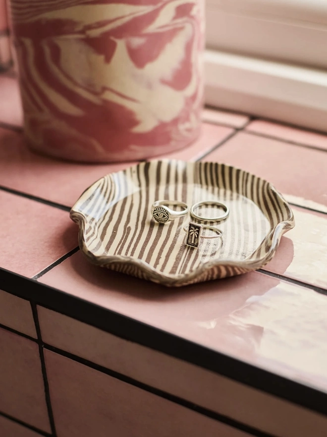 Striped Trinket Dish, a colourful trinket dish on a window sill. It is accompanied by some rings. 