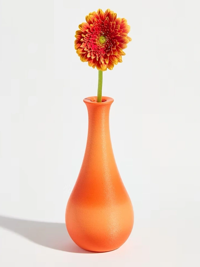 tear shaped bright orange 3d printed vase holding orange flower