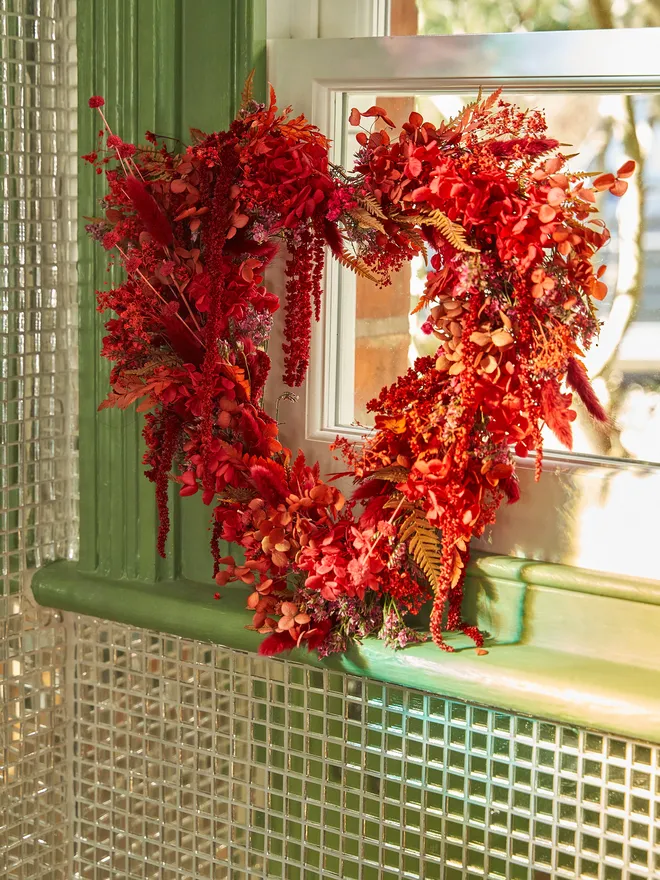 Red floral heart wreath lent against a green windowsill set in a disco ball tiled wall with sunlight streaming in