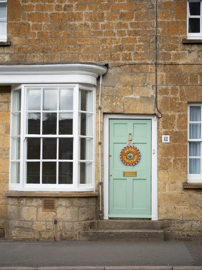 Multicoloured Hand painted Christmas Wreath with gold leaf lettering on a pale green front door old house