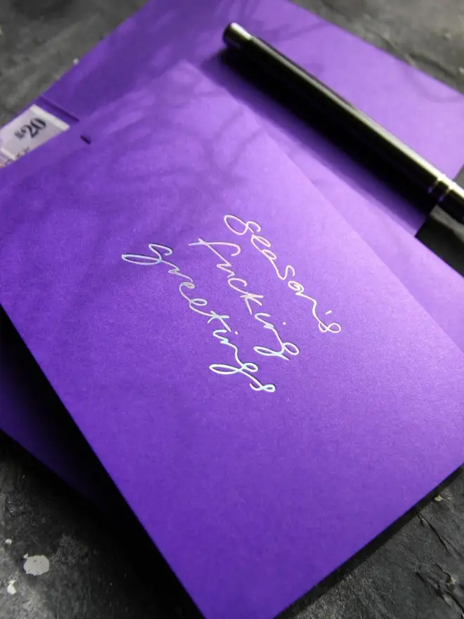 Hand foiled cash card or money wallet in a royal purple colour handfoiled in shiny holographic text which says 'season's fucking greetings'.