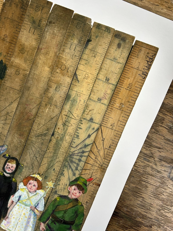 signature of artist on print of children in fancy dress painted onto vintage school rulers