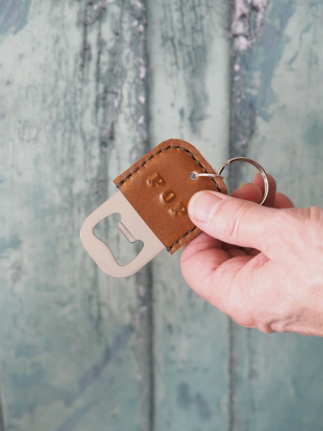 personalised tan brown leather bottle opener key ring. Held in a hand the leather is stamped with the name POP