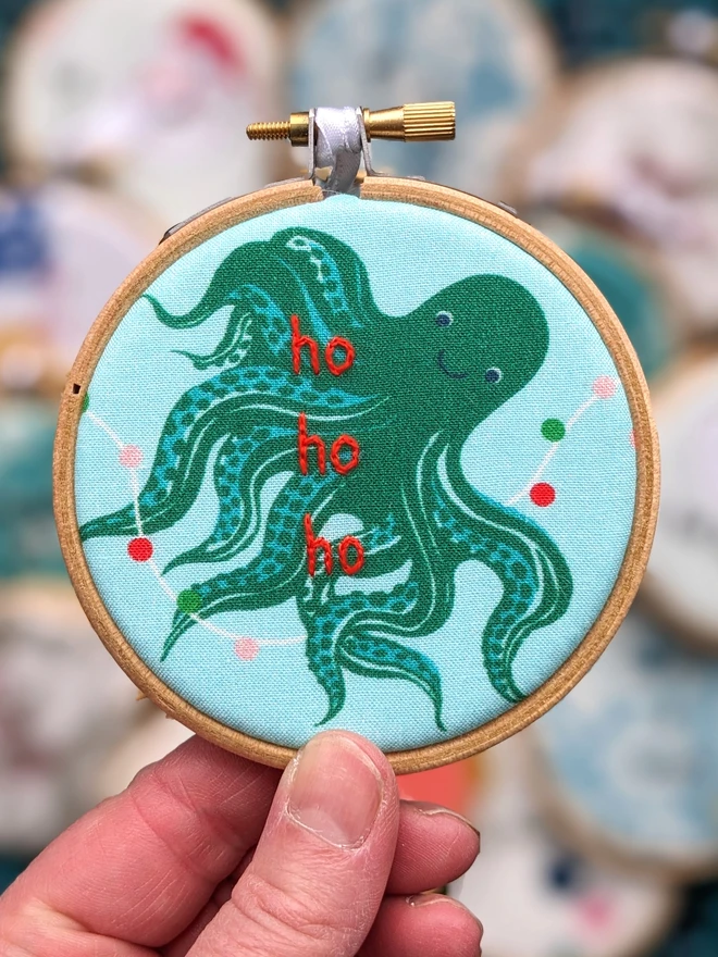 A hand embroidered hoop on Christmas fabric reading ho ho ho