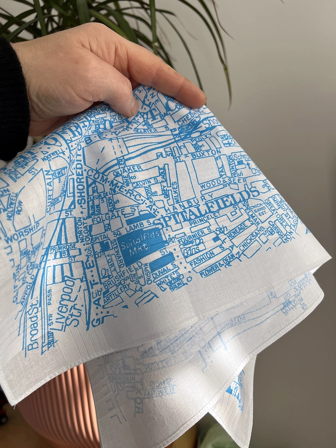 A hand holds a Mr.PS East London map handkerchief in front of a pink plant pot